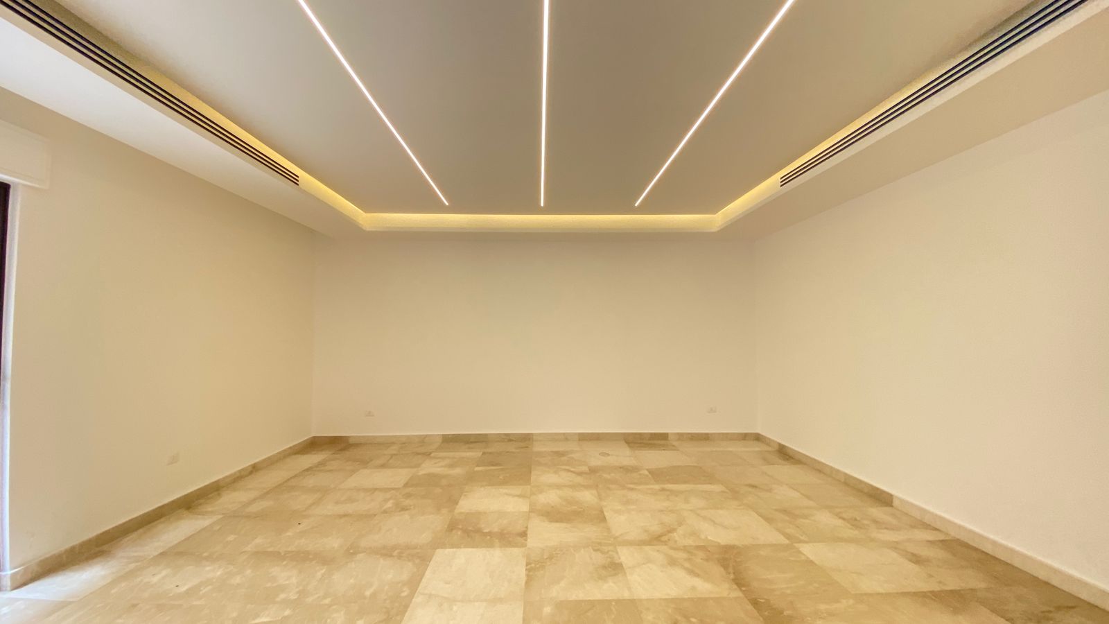 4db9a779-5f2a-441a-8841-d62f5e82514f Empty rectangular room with beige marble tile floor and modern ceiling LED lights along the edges.