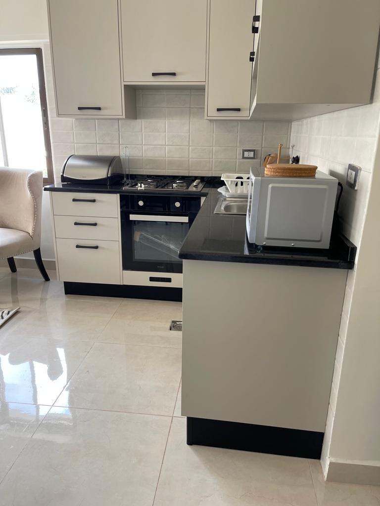 4f47e369-456b-41a9-8312-6b82891e8b29 Modern L-shaped kitchen with white cabinets, black countertops, gas range and built-in oven; microwave on the counter.