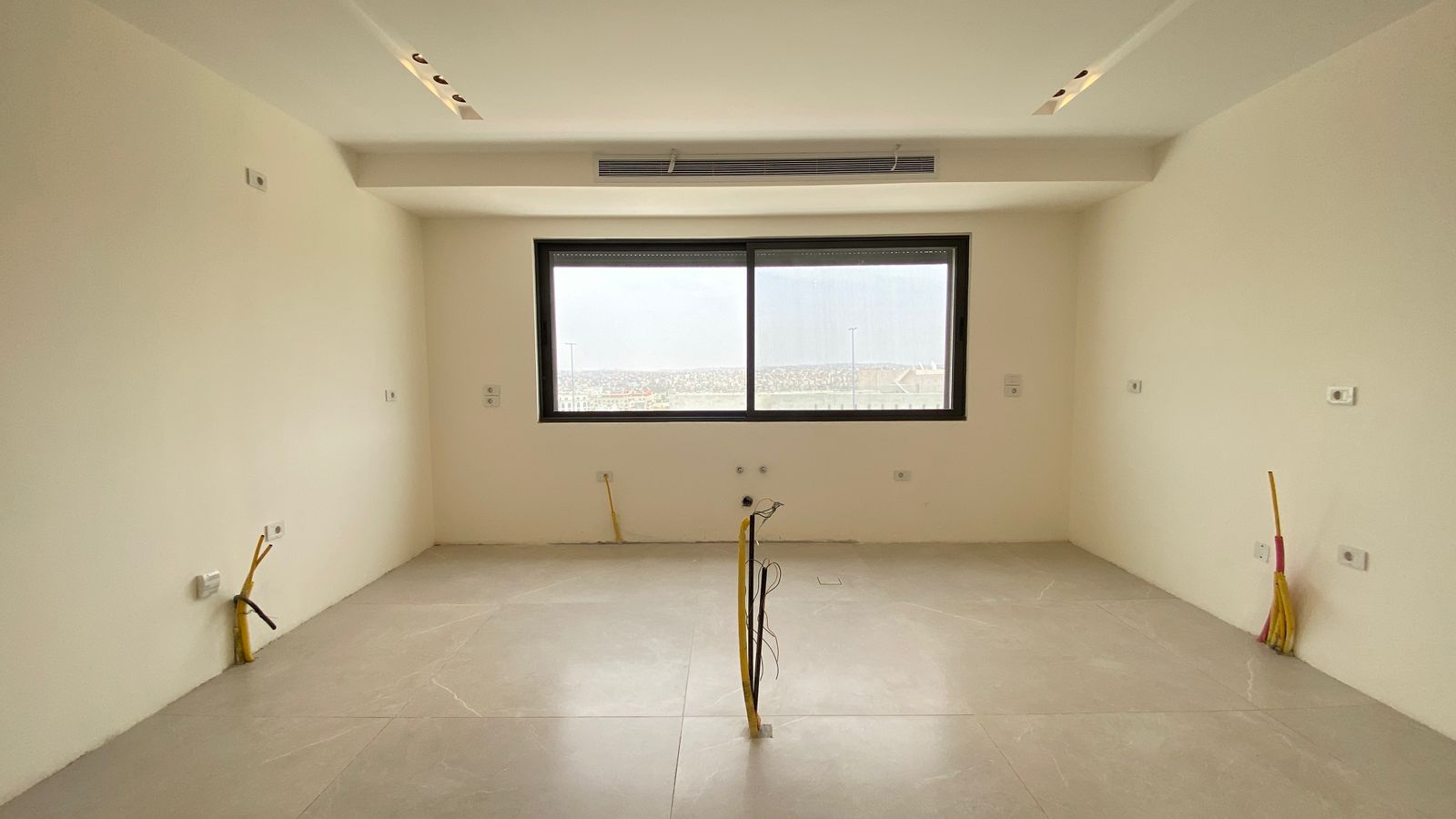 527aa0e3-7c7e-419d-8719-a352d9b61b69 Empty unfinished room with exposed electrical wires in floor and walls, large window with city view.