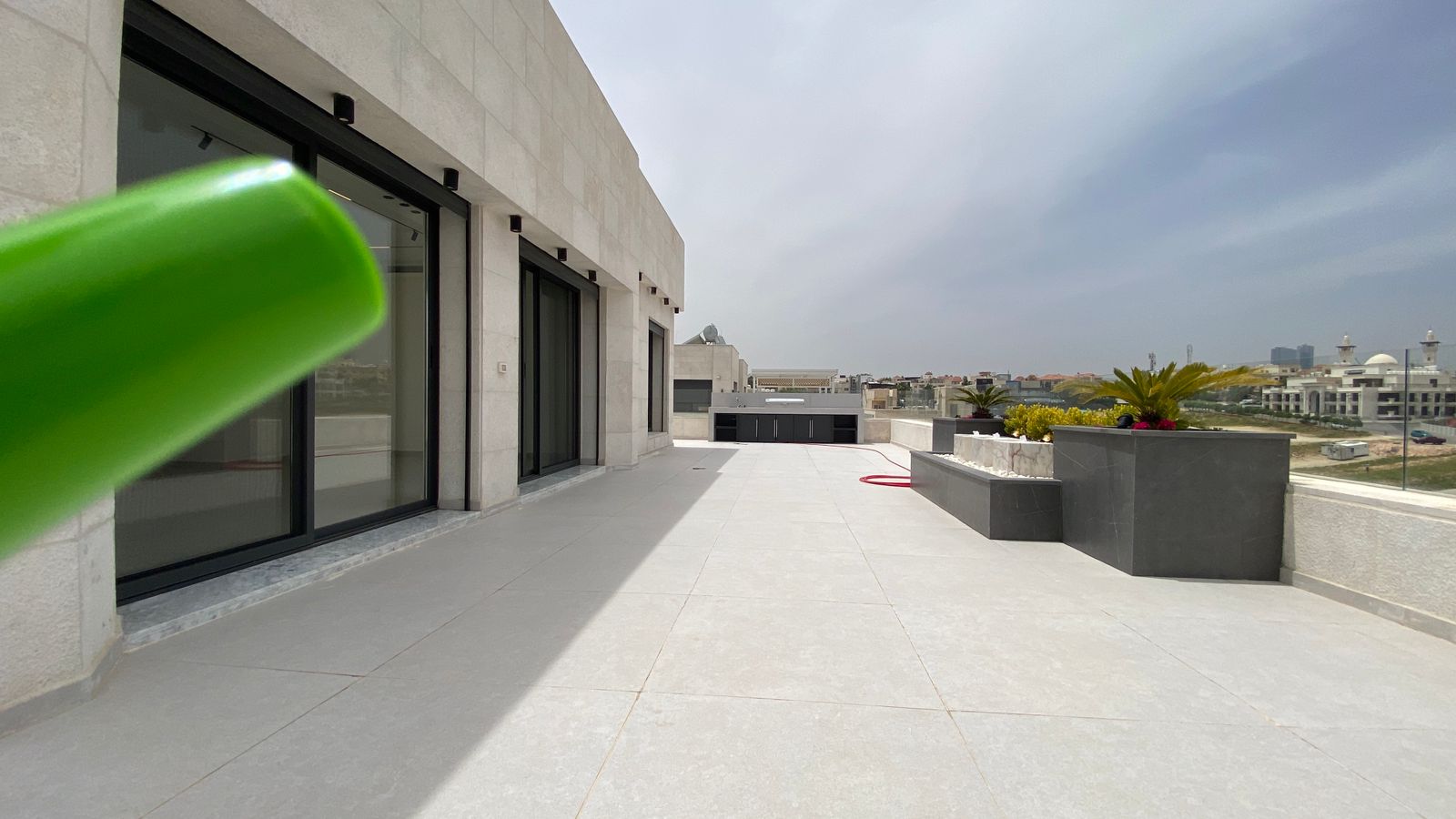 53787bf0-7ba6-4932-976c-2c7107516c4e Modern rooftop terrace with pale stone walls, large sliding glass doors, and raised planters; city skyline on the horizon.