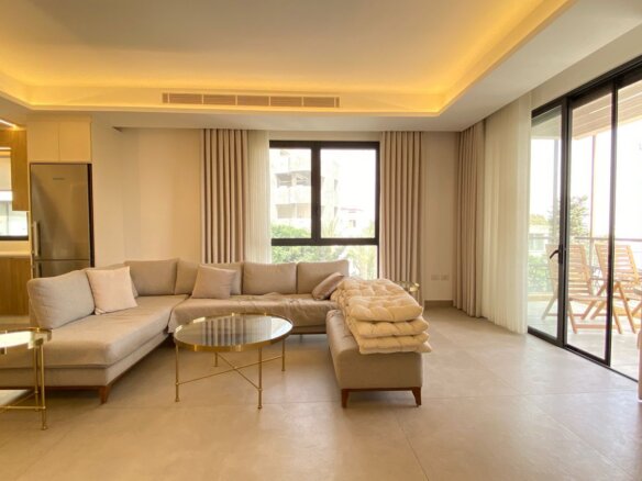 Open-plan living room with a curved L-shaped beige sofa, round glass coffee tables, and beige curtains.