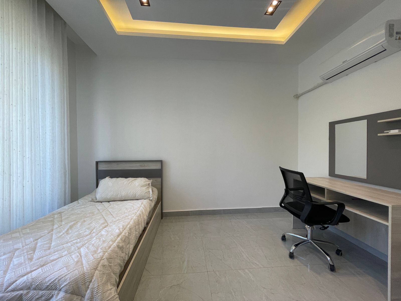 555f22e7-2624-48ae-9a90-3055c99e5c71 Minimalist bedroom with a single bed on the left and a desk with chair on the right, neutral tones and soft lighting.