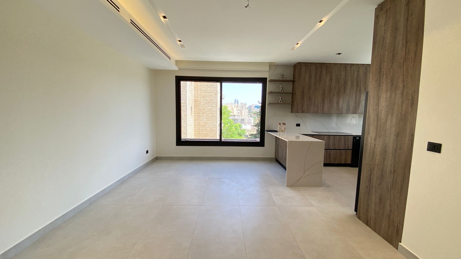 58c3c56f-0878-4a97-a763-79b925f773c6 Open-plan living area with a white marble island and wood-finish cabinets; large window overlooks the city/trees outside.