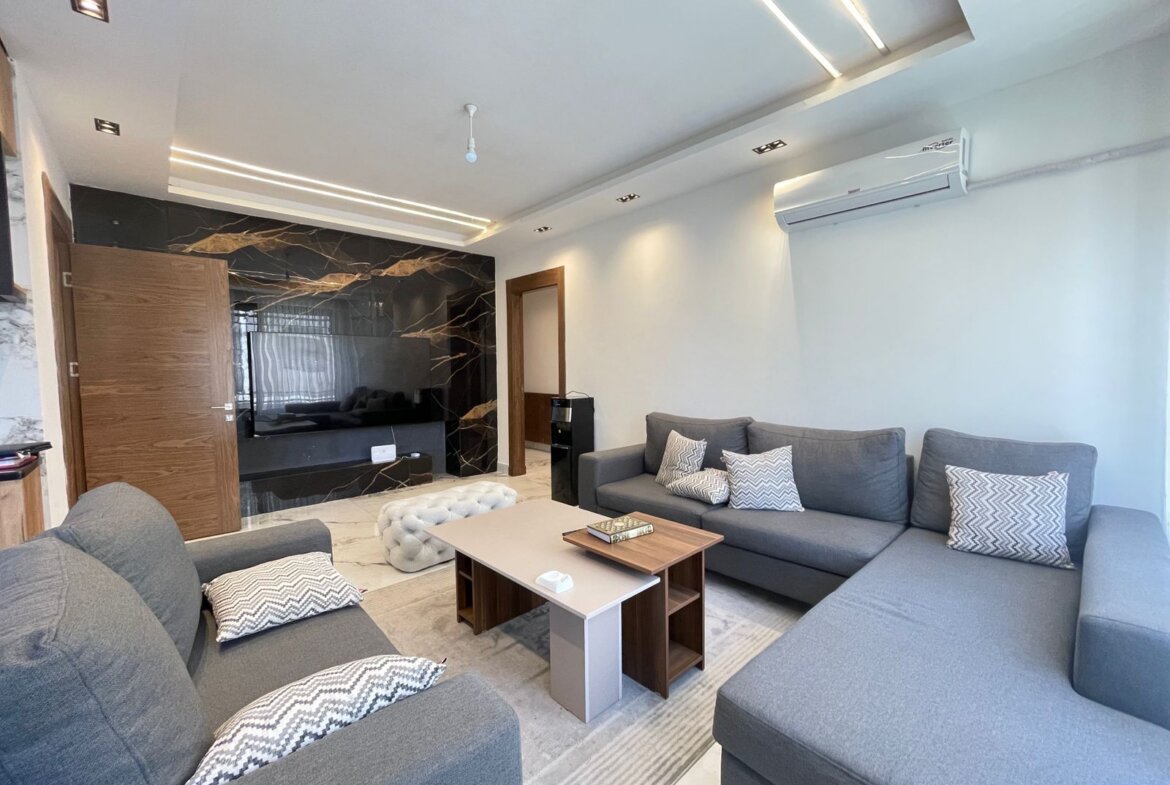Open living room with a large gray sectional sofa, chevron pillows, and a marble-accent wall with a mounted TV.