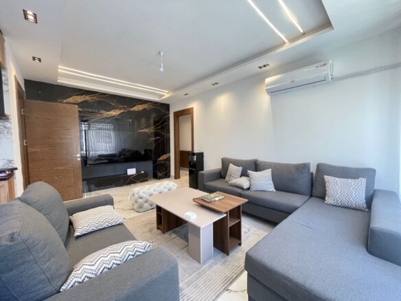 Open living room with a large gray sectional sofa, chevron pillows, and a marble-accent wall with a mounted TV.