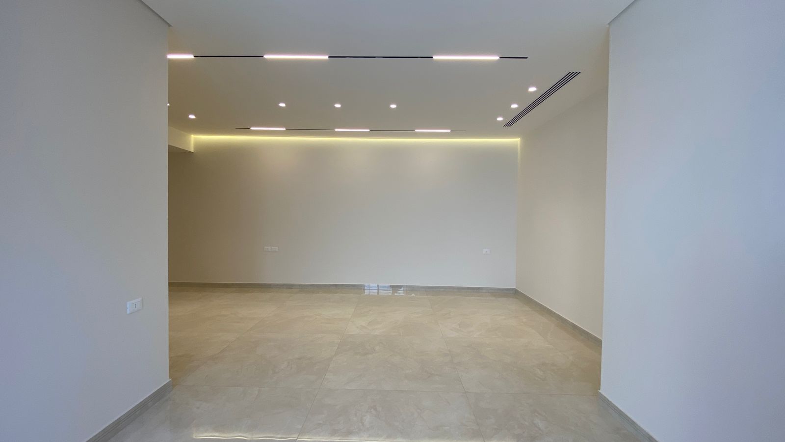 5a7899ea-a227-4a4a-a169-7ab63d461c2f Empty modern room or showroom with pale walls, large light tiled floor, and recessed ceiling lights providing even illumination