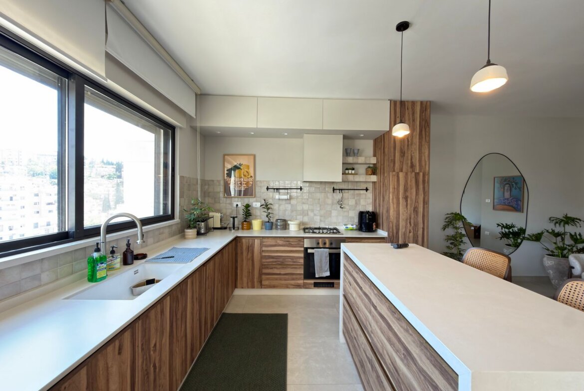 Bright, modern kitchen with woodgrain cabinets, white countertops, and a large window along the sink wall.