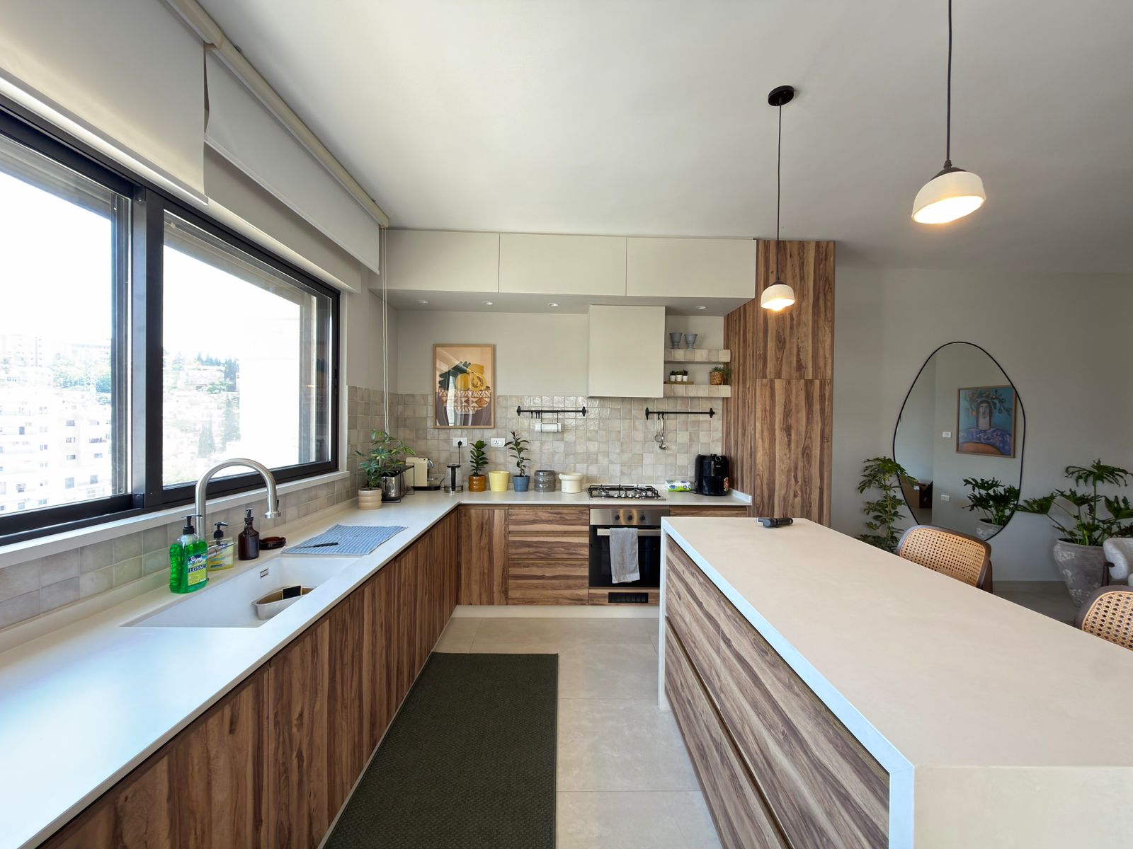 5b6318b0-a902-4d98-a062-63adadc3e478 Bright, modern kitchen with woodgrain cabinets, white countertops, and a large window along the sink wall.