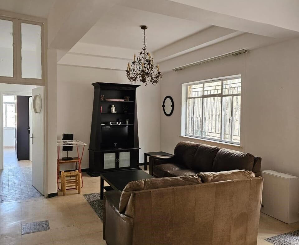 Living room with brown sectional sofa, black bookshelf, chandelier, and a large window.