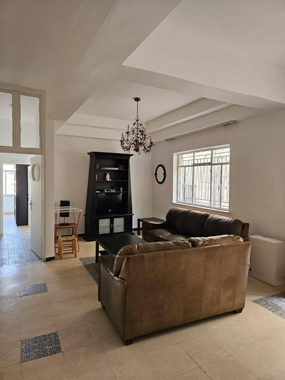 5bad554b-d1e0-434d-8377-fab250034c78 Living room with brown sectional sofa, black bookshelf, chandelier, and a large window.