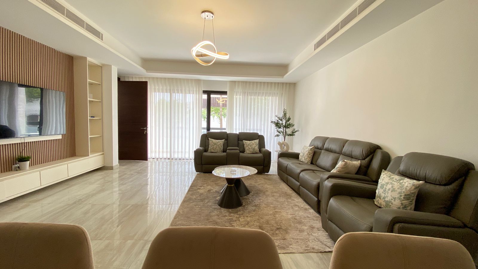 5ff27ce8-85d3-46ab-99fc-cf11013026d8 Spacious living room with gray leather sectional, matching loveseat, round coffee table, and a rug near glass doors with sheer curtains.