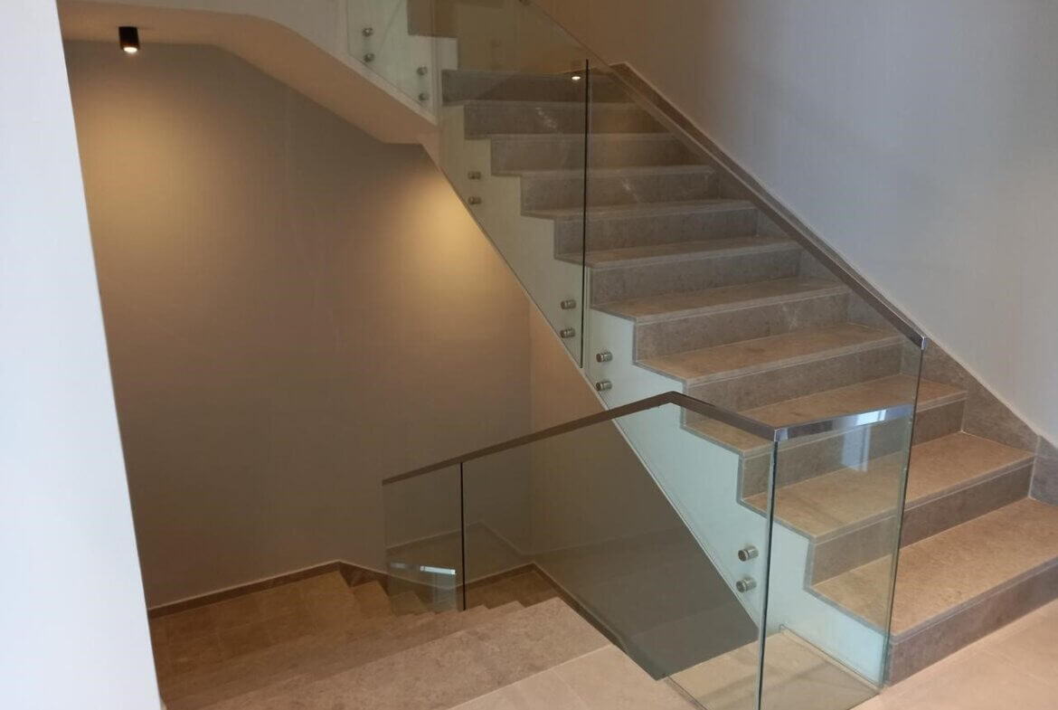 605ef811-6551-4b5a-b888-87e3587cfab3 Modern indoor staircase with beige steps and a glass railing, leading to an upper floor in a neutral-toned interior.