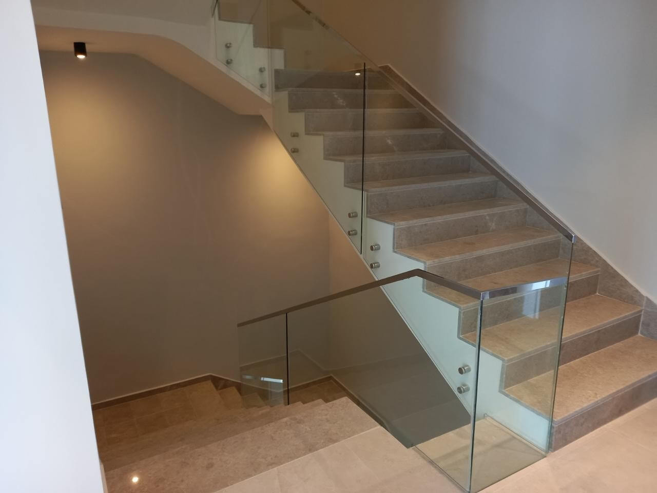 605ef811-6551-4b5a-b888-87e3587cfab3 Modern indoor staircase with beige steps and a glass railing, leading to an upper floor in a neutral-toned interior.
