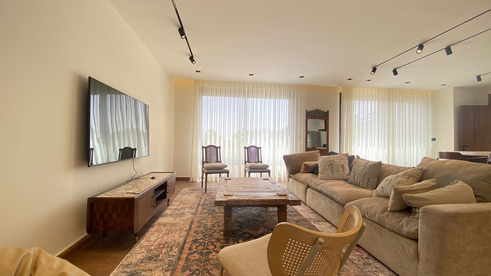 60f71769-b4c6-4651-bdda-b43211051c93 Spacious living room with a wall-mounted flat-screen TV, wooden media console, and beige sectional sofa facing the screen.