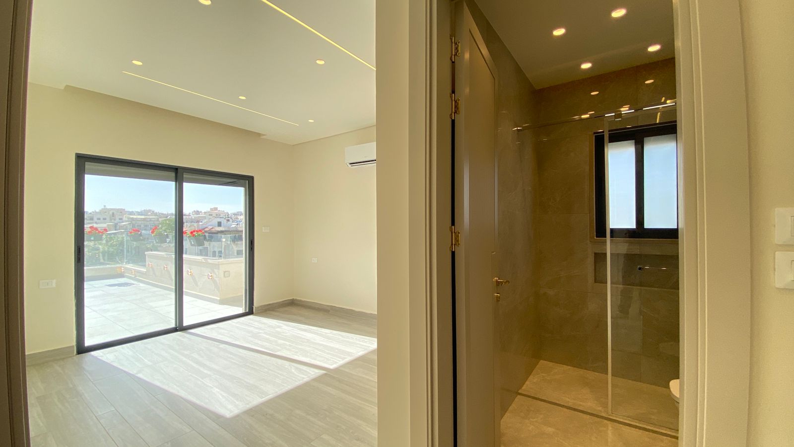 635575a5-075d-4290-a8d3-ef9a695e9031 Bright living area with a large sliding glass door to a balcony and city views; sunlit gray tile floor and beige walls.