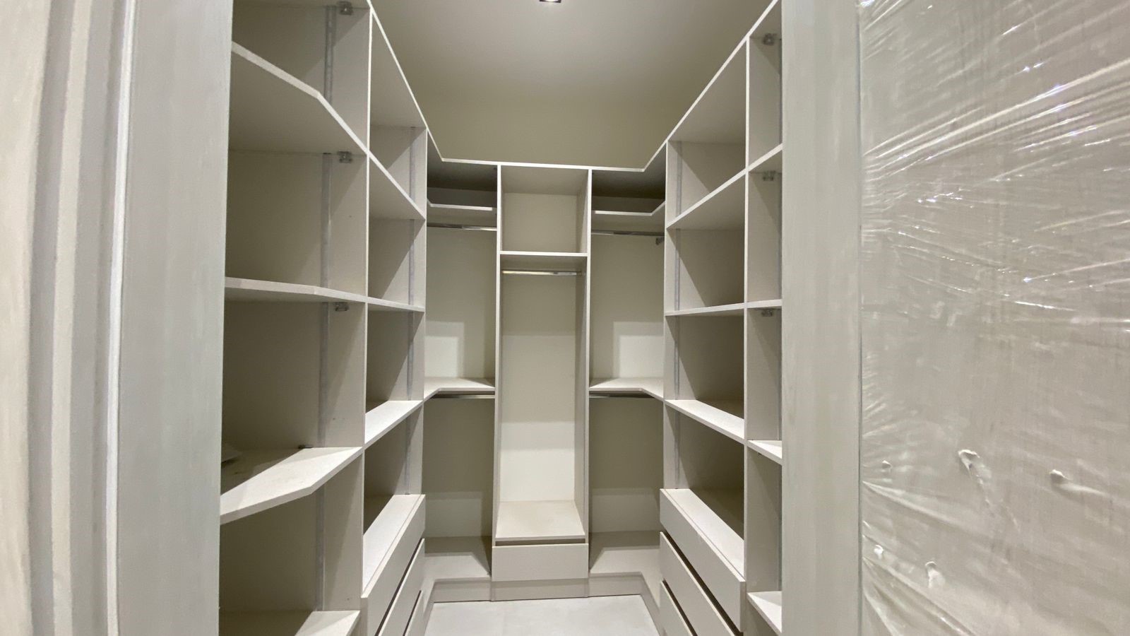 63703a2d-f29c-4830-84e0-7bf8a176f06d Empty walk-in closet with white built-in shelves and drawers, symmetrical storage around a central aisle