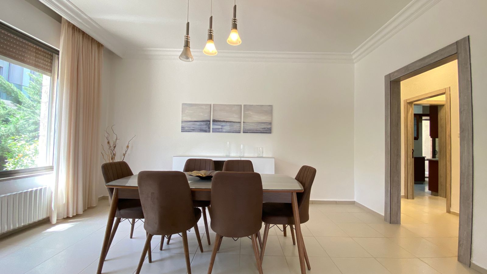 63d6e7e2-f902-4104-a914-ad8f14b24573 Modern dining room with a glass-topped table surrounded by six brown upholstered chairs and warm pendant lights.