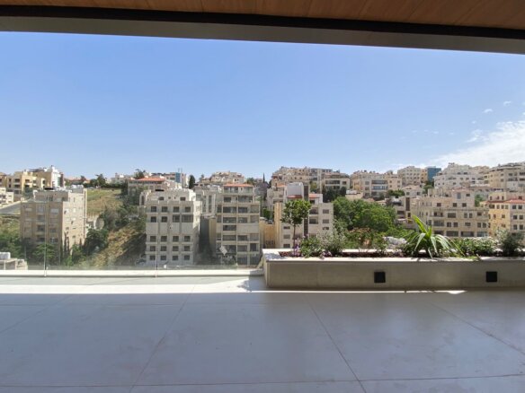 Balcony with a planter box overlooking a city of beige apartment buildings and green hills under a clear blue sky.