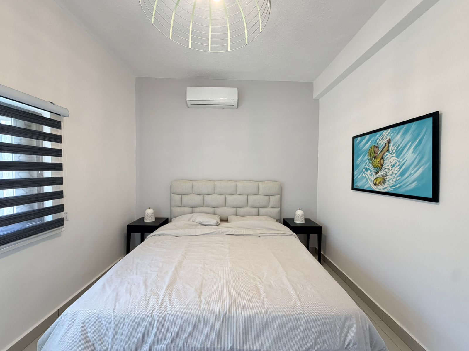 667668f7-809a-4c09-8eac-a75ce0a958ec Bedroom with a centered tufted headboard, white bedding, black nightstands, and matching lamps on both sides.