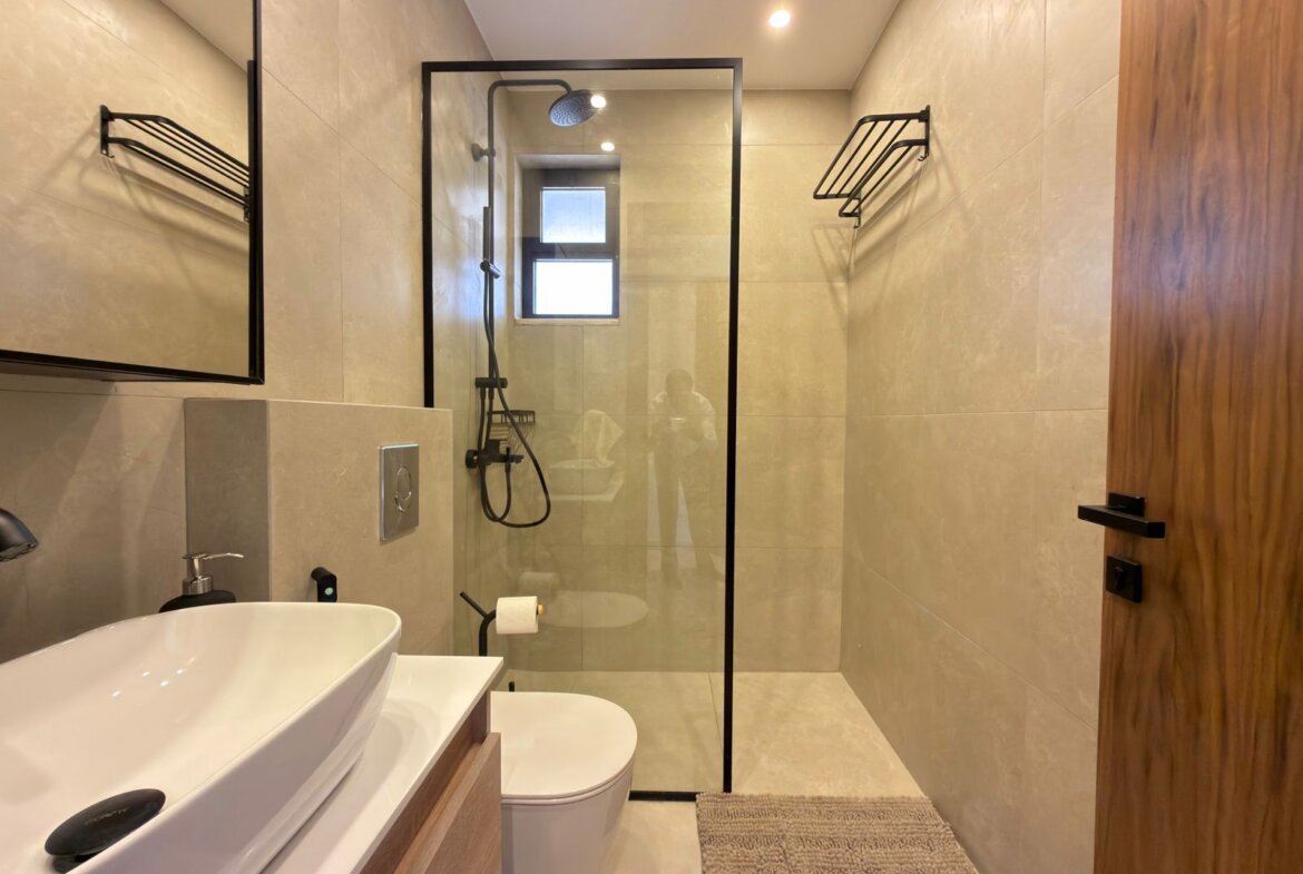Modern bathroom with a glass shower enclosure, beige tile walls, and a white freestanding sink on a wooden vanity.