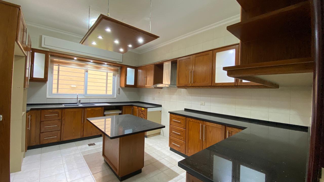 6d6a113f-ae8e-4ccf-adc9-ff721a308773 Bright kitchen with wooden cabinets, black countertops, and a central island under a modern ceiling light.