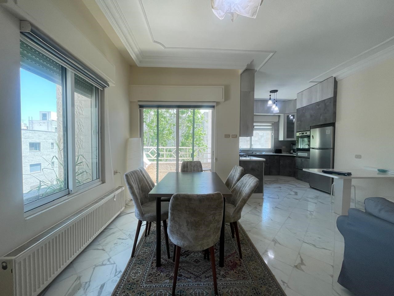 71cd0ace-247c-484b-b494-7b1188c624c7 Open-plan dining area with a dark wood table and six upholstered chairs, adjacent to a modern kitchen with stainless appliances.