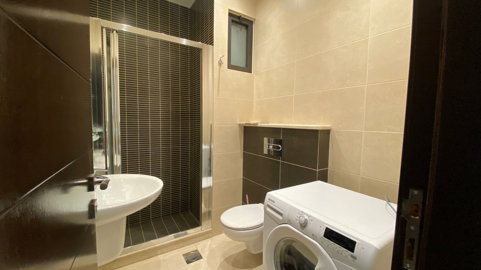 73f518aa-82e7-4f47-8675-dbca56919d35 Small modern bathroom with a walk-in shower, white sink, toilet, and front-loading washing machine.