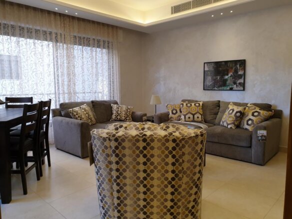 Living room with a gray sectional sofa, multiple patterned cushions, and a hex-patterned chair in the foreground.