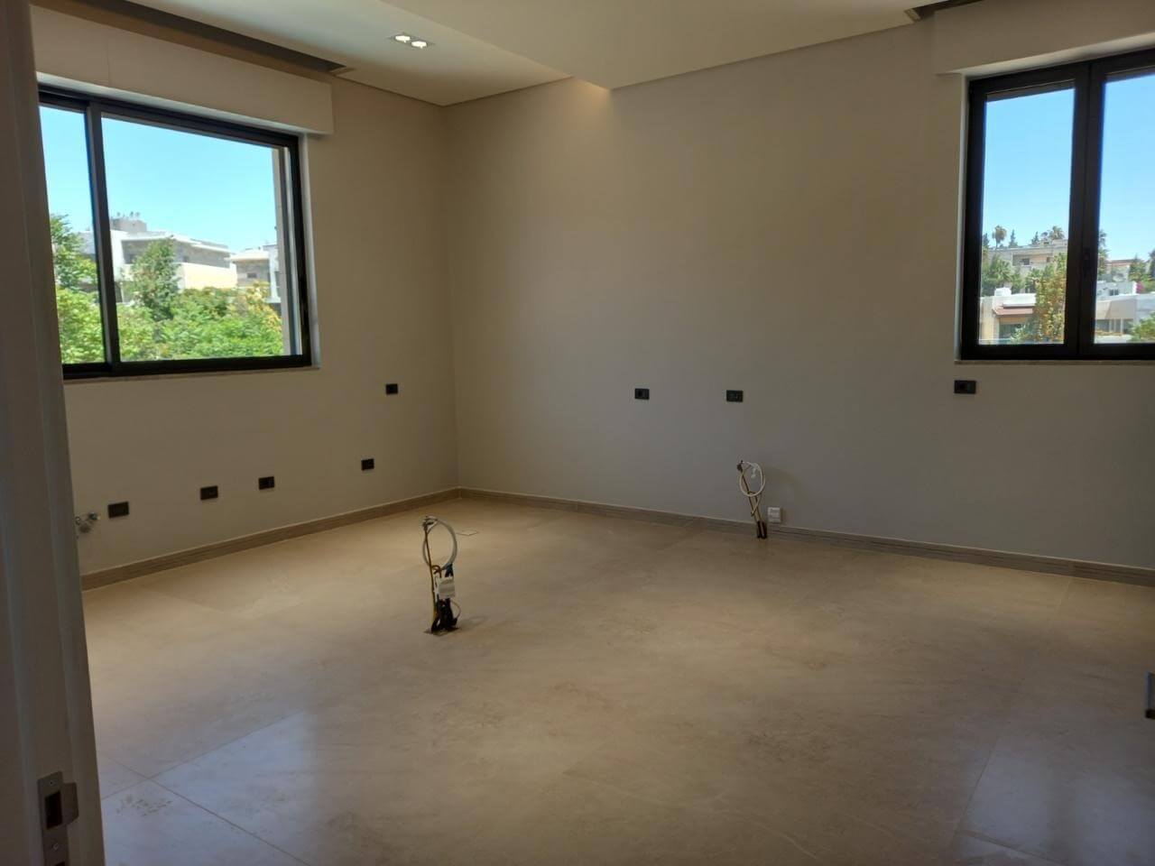 800bee2d-364a-4ea4-bfb9-5492ba309b31 Empty, unfurnished room under construction with two large windows and visible electrical outlets/wires on walls and floor.