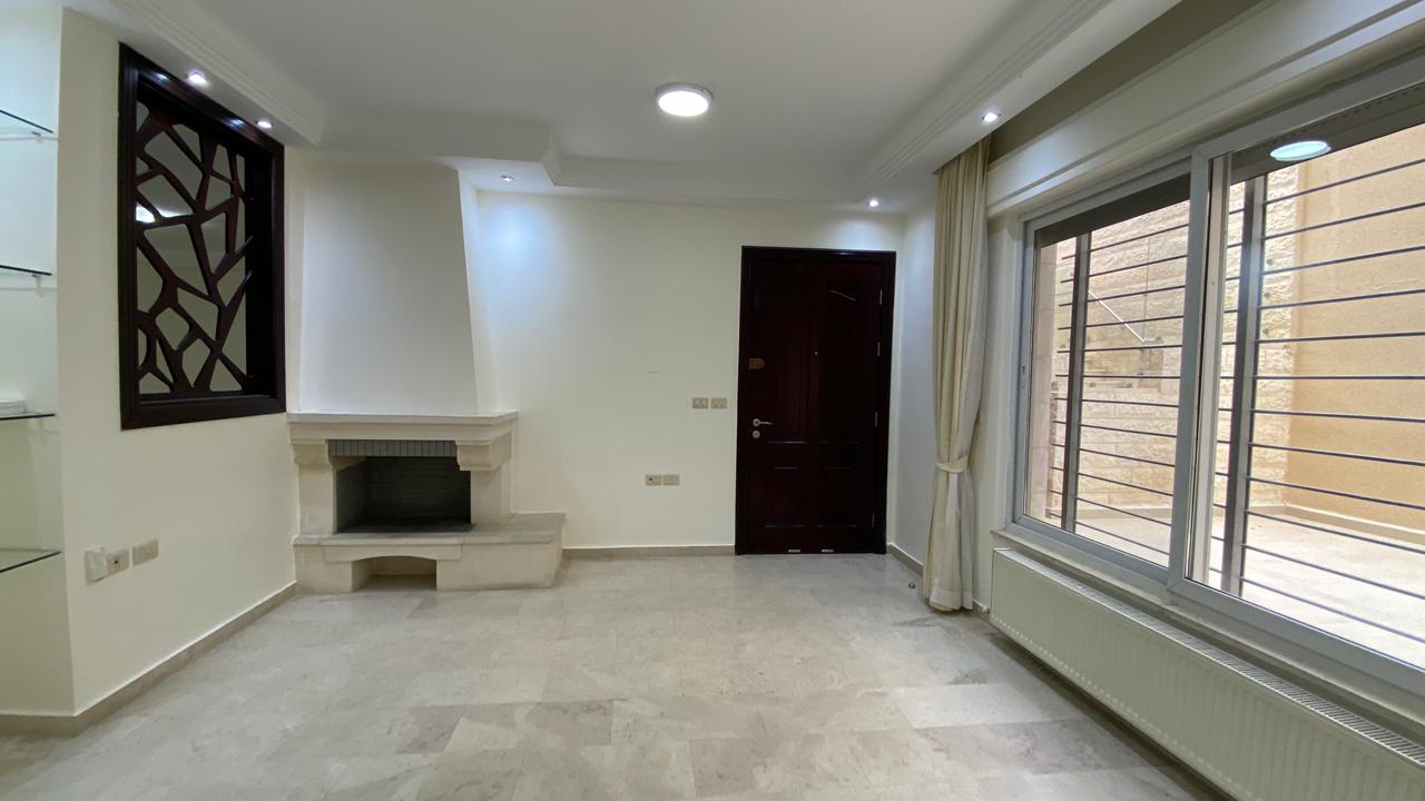 816850c6-481f-4b21-901c-7872927612e1 Modern living room with white walls, a stone fireplace, large window with beige curtains, and a dark entry door.