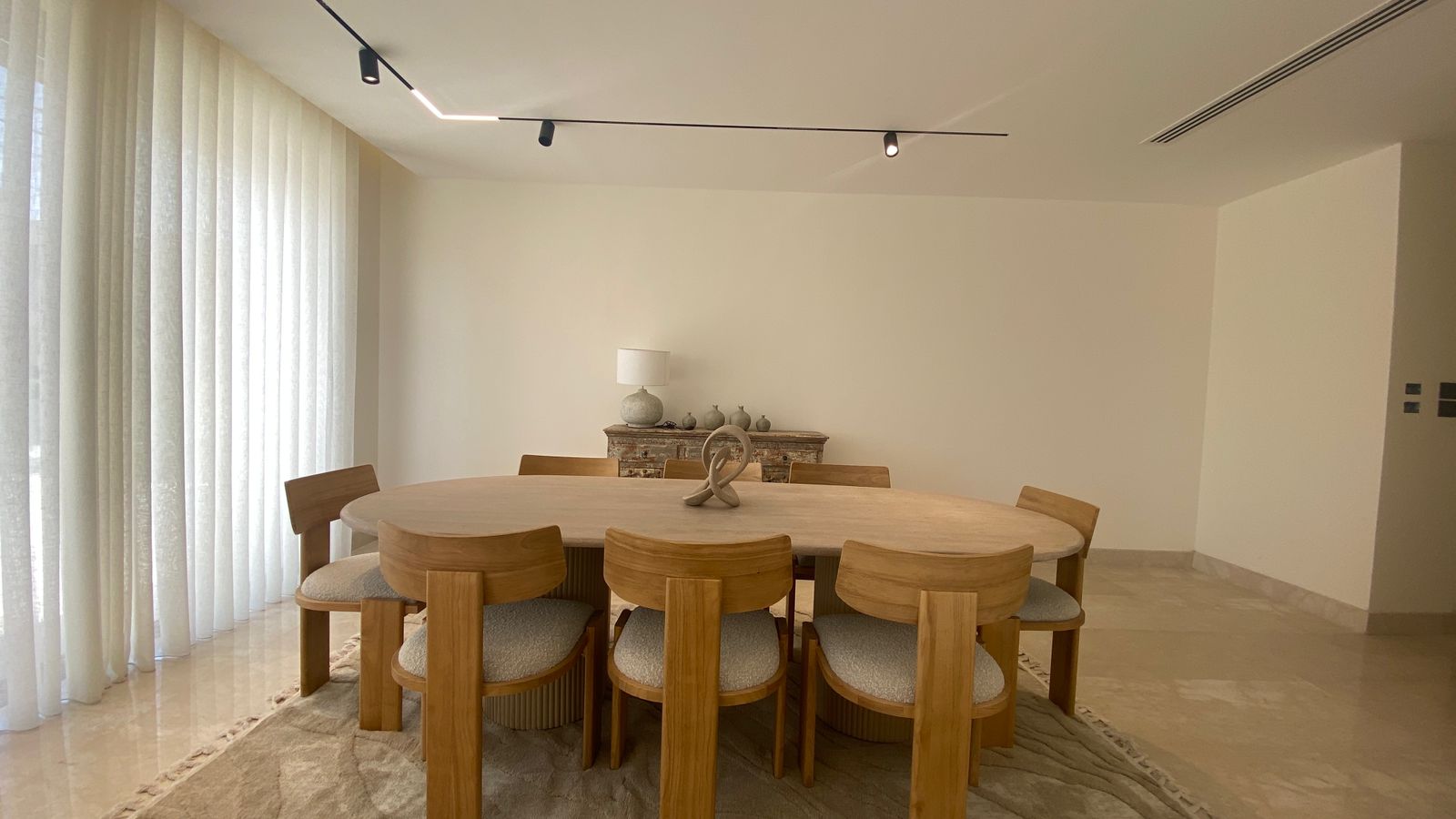 823ef51b-81e9-4c2d-b586-c2954072d252 Round wooden dining table with eight matching chairs in a bright minimalist dining room.