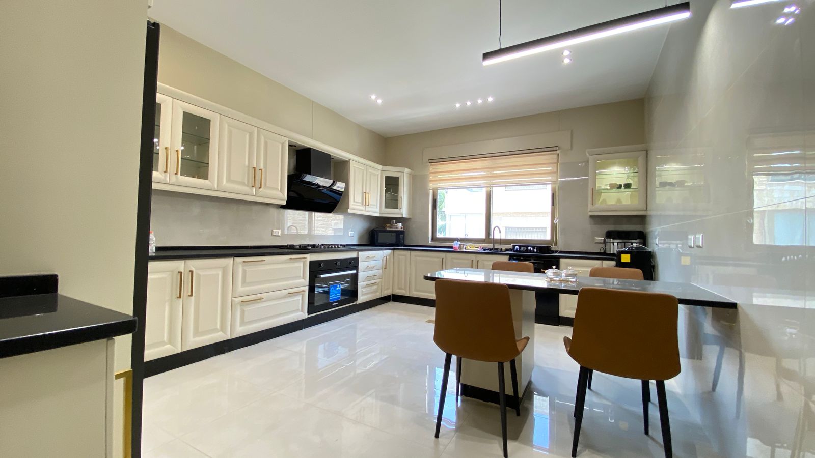 828e7f43-d444-4a8f-a67f-0c9ad001733f Bright modern kitchen with white cabinets, black countertops, built-in oven, and a rectangular dining table with brown chairs by a window.