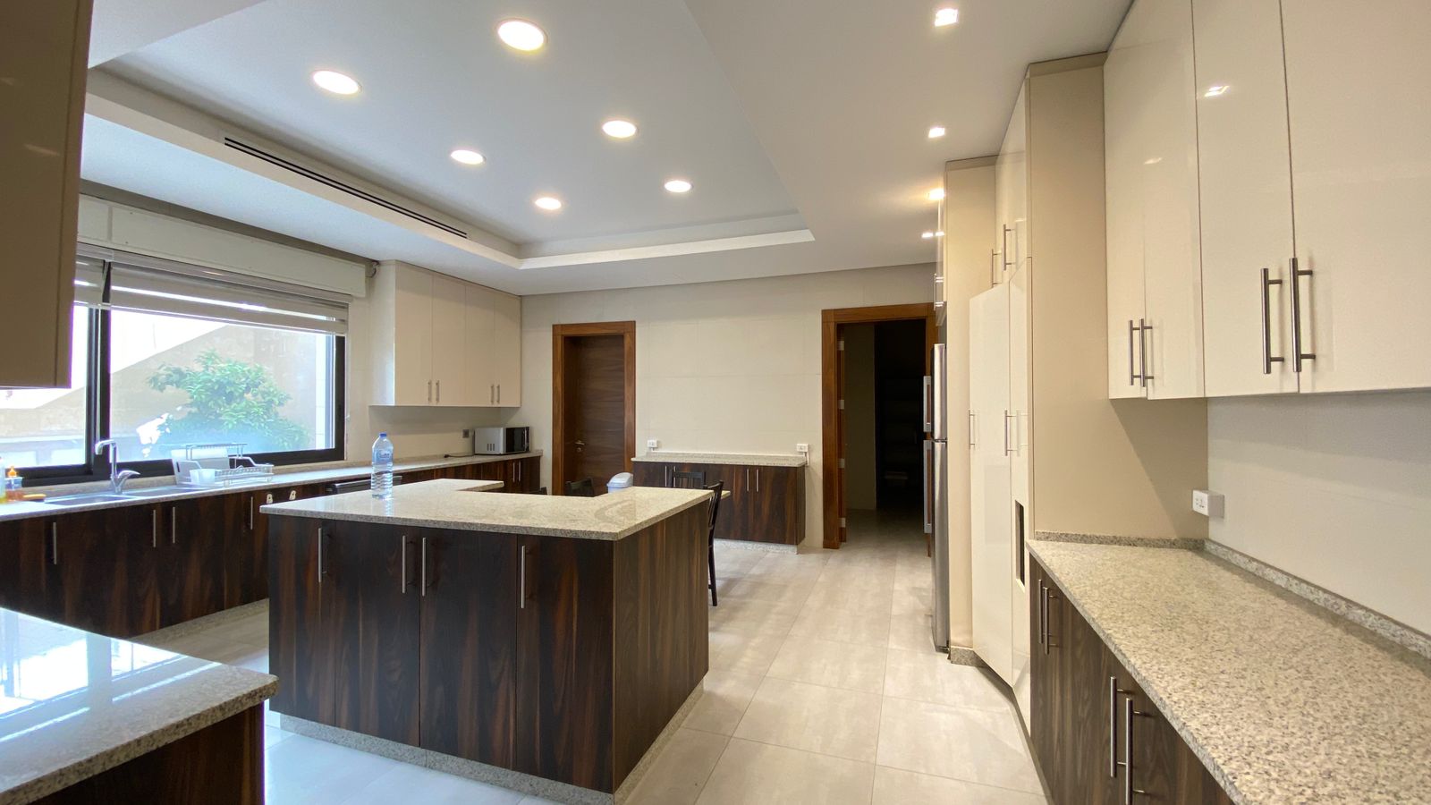 87a87993-aa2e-4af3-91ef-d347142aa9eb Modern kitchen with an island, dark wood lower cabinets, light upper cabinets, granite countertops, and stainless appliances under recessed lighting.