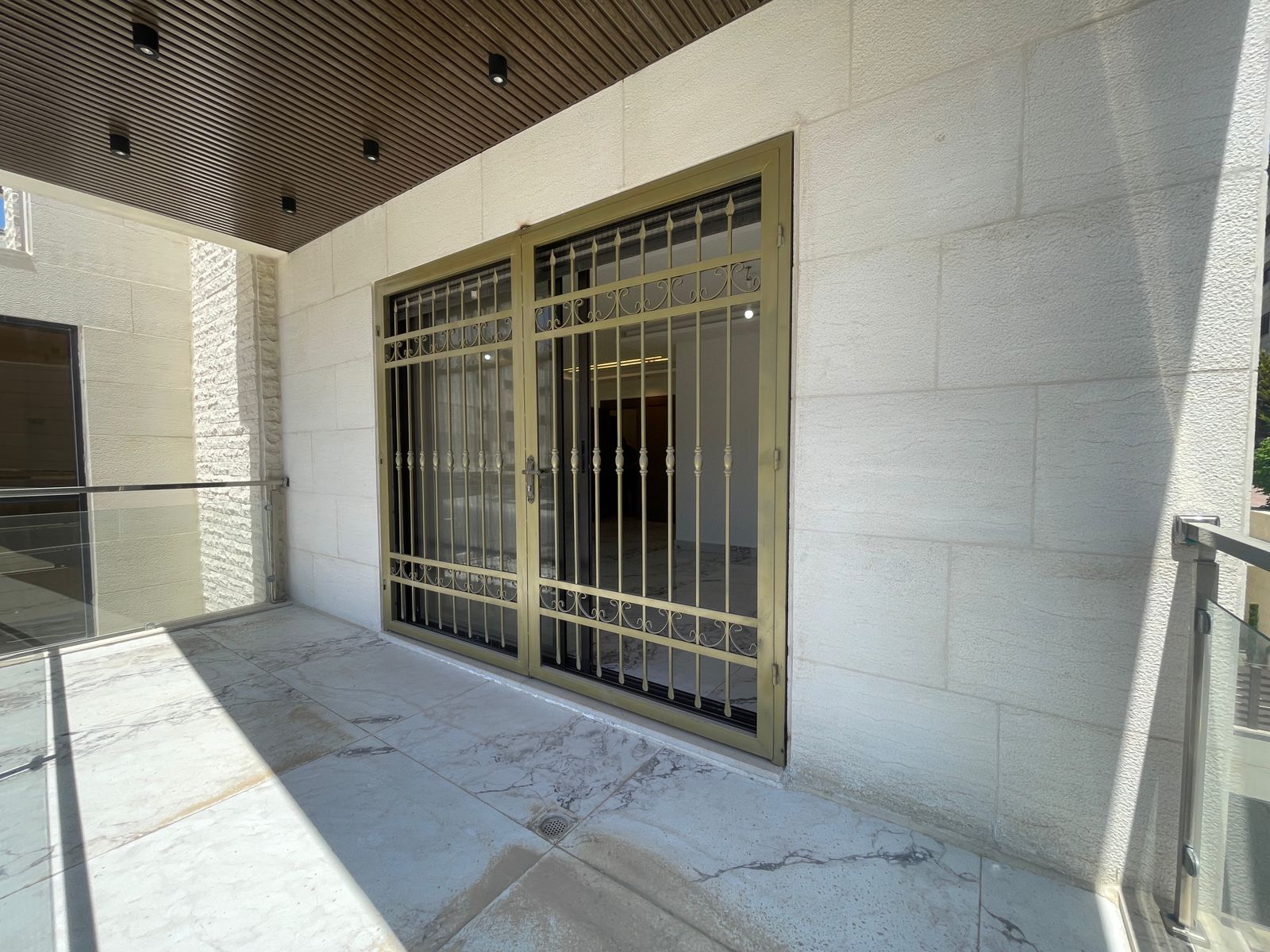 881ba3d6-af43-44ae-82ac-e40d45cae3c8 Gold-toned decorative security gate blocking a doorway on a white marble balcony exterior.