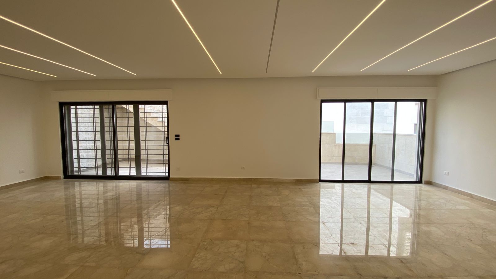 8bacfa38-2f5d-4974-b7d6-1d3b253a31f3 Spacious, unfurnished living room with marble floors and two large sliding doors opening to a balcony; recessed linear LED ceiling lights.