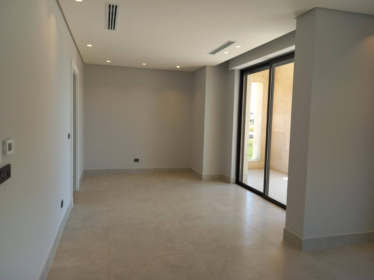 8d755a7f-99bc-40f8-953e-c1862890ca39 Empty modern living area with large sliding glass doors to a balcony, neutral gray walls, and light tiled floor.