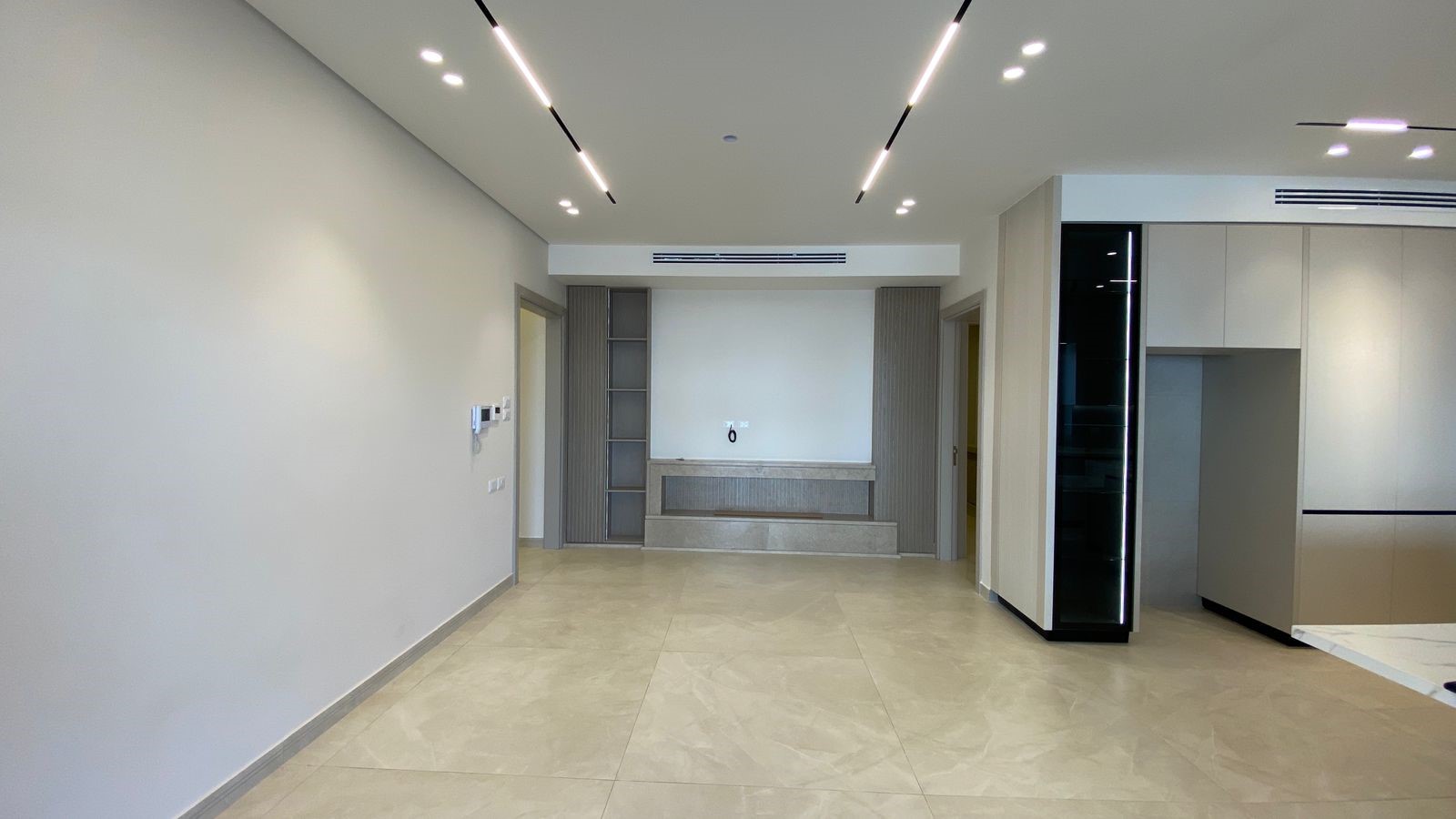 9550c7dc-172a-4ecb-b471-733509d91f0c Empty modern open-plan living area with beige tile floor, gray walls, and a built-in console along the back wall.