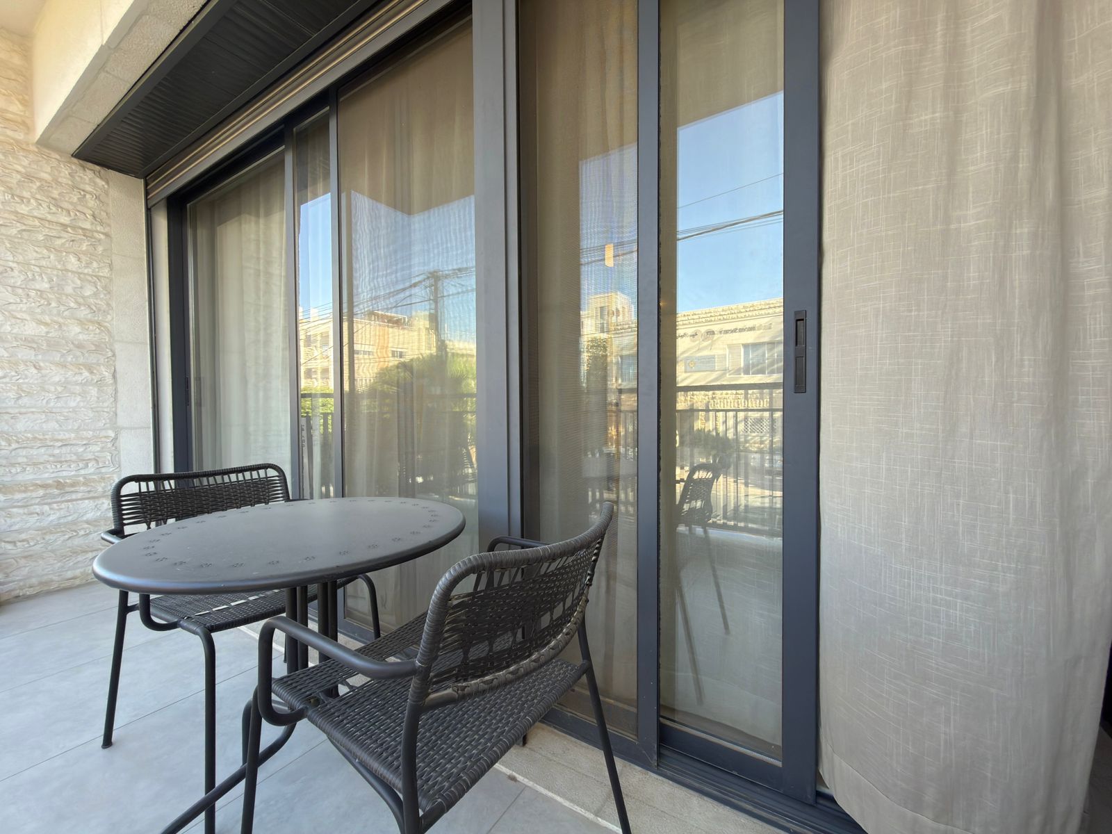 991f98f2-8c3f-46d4-9d75-a68c7acaf7a6 Outdoor balcony with a round metal table and two wicker chairs facing glass sliding doors