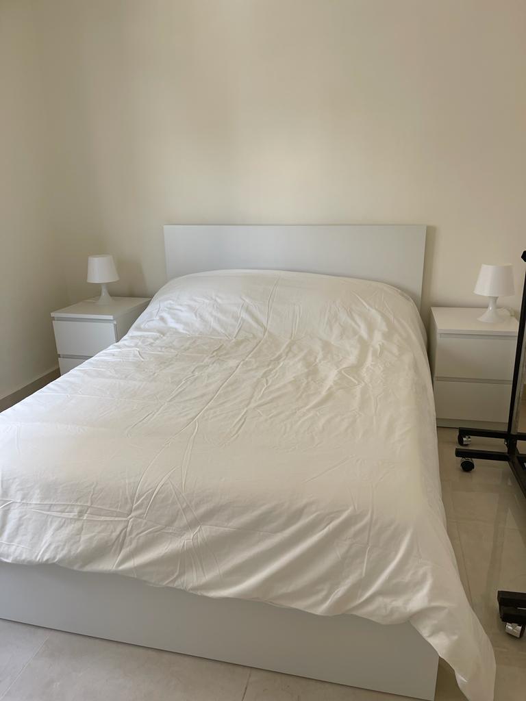 9eb2a1f2-a519-4be7-b434-2f1757dc7247 Minimal white bedroom with a neatly made bed, white headboard, and matching white nightstands with lamps on each side.