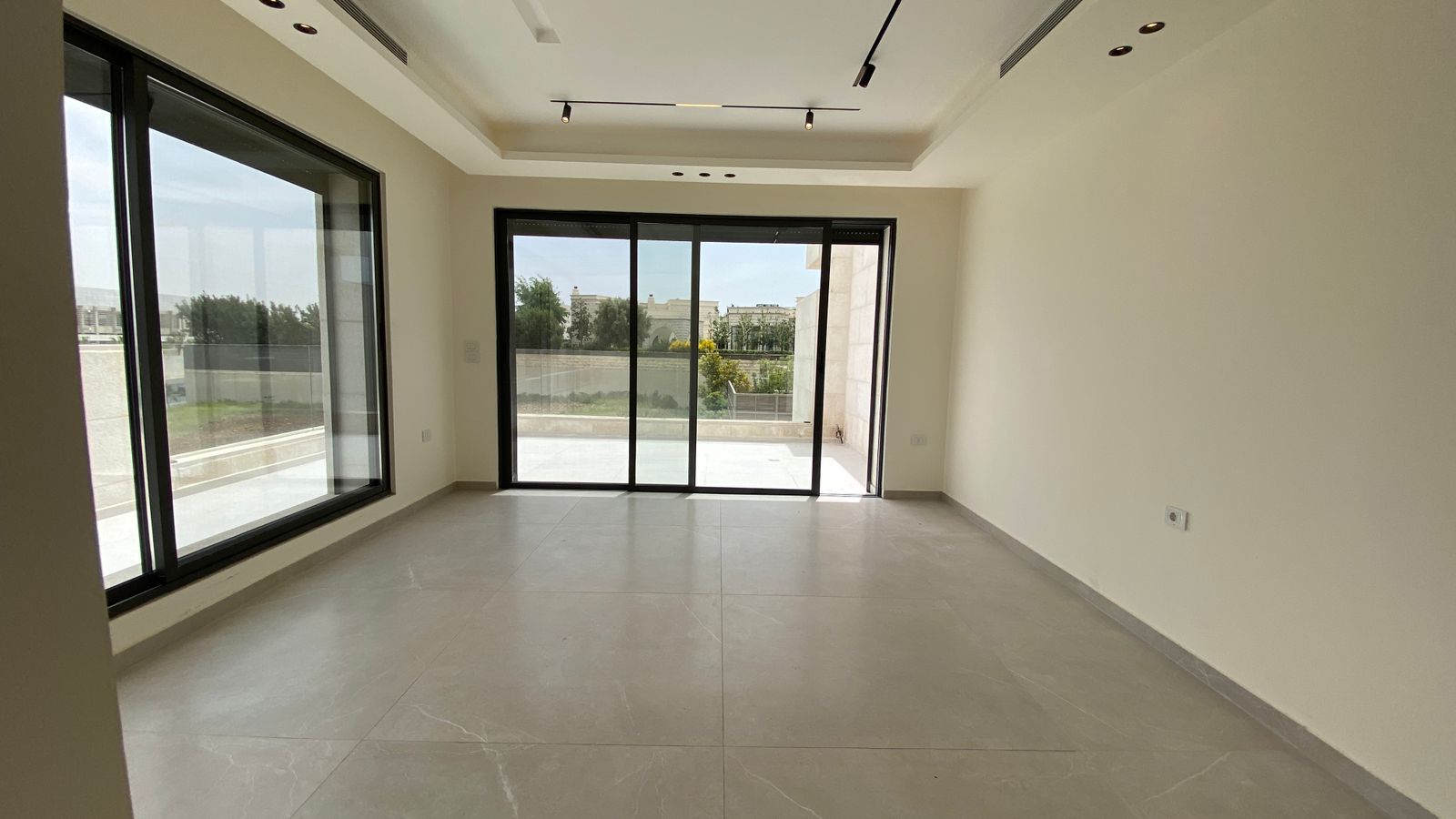 a179e6e7-46e3-469d-84bc-a4c41afc364d Bright empty living room with large glass sliding doors to a balcony and a floor-to-ceiling window; gray tiled floor.