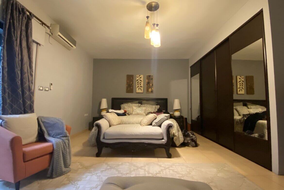 a1a9504e-6f1f-4513-ae51-2679c4b0cedd Bedroom scene with a dark wood bed on a gray accent wall, two matching bedside lamps, and a white cushioned sofa at the foot of the bed