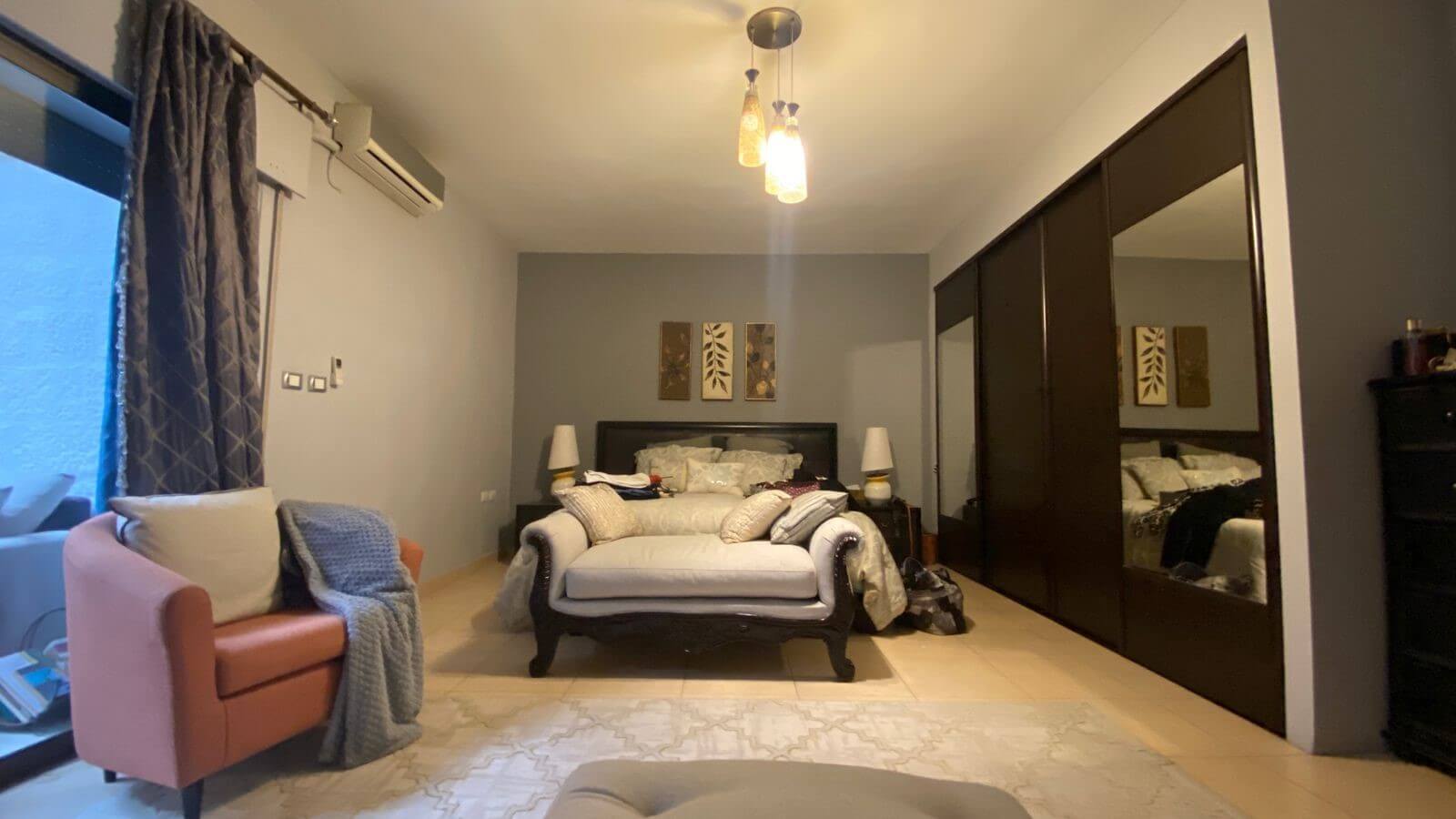 a1a9504e-6f1f-4513-ae51-2679c4b0cedd Bedroom scene with a dark wood bed on a gray accent wall, two matching bedside lamps, and a white cushioned sofa at the foot of the bed