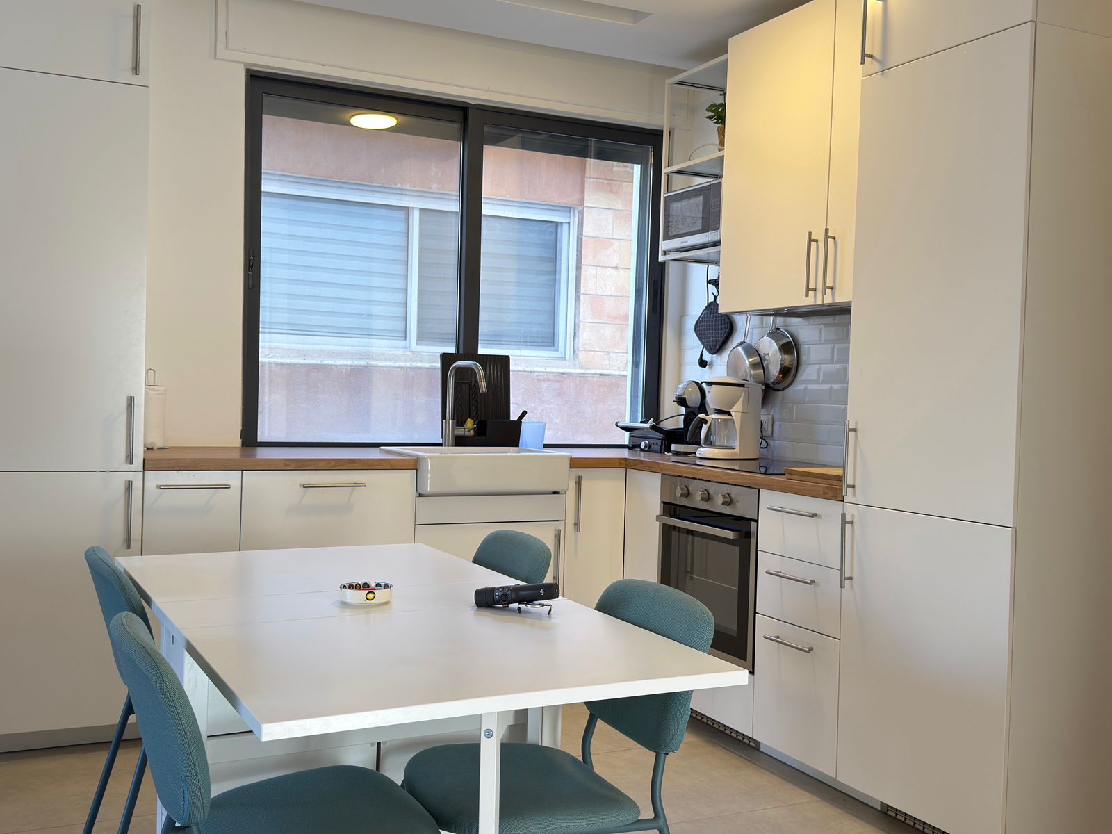 a211fbcd-2b50-41dd-b5c0-93191af0bc0e Modern white kitchen with a wooden countertop, white dining table, and blue upholstered chairs beneath a large window over the sink.