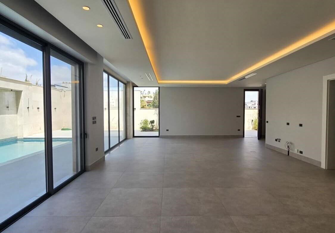 a23ed9bb-6b6b-4b9c-bd6d-1c83aec142c4 Empty modern living room with large glass sliding doors opening to a pool area and gray tiled floor.