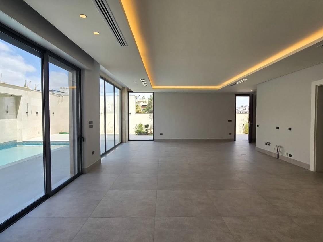 a23ed9bb-6b6b-4b9c-bd6d-1c83aec142c4 Empty modern living room with large glass sliding doors opening to a pool area and gray tiled floor.