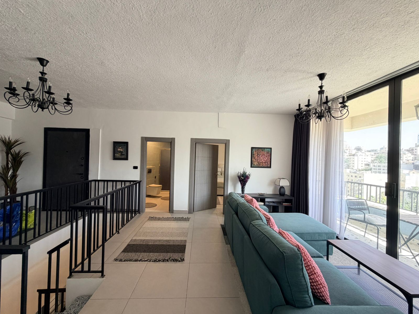 a5222859-d63d-41af-a637-acd164f3f900 Open-plan living room with a teal sectional, large glass doors to a balcony, and a city view outside.