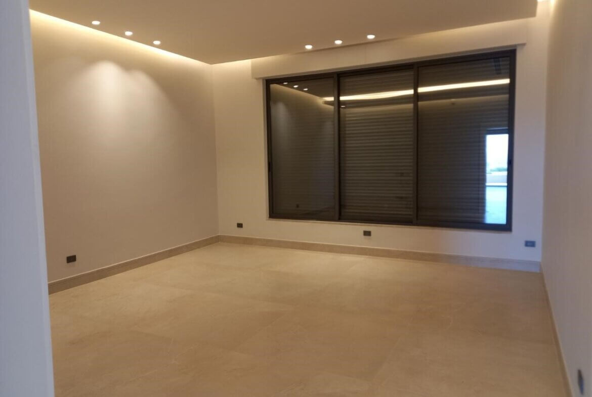 a71aa486-c872-477a-b37a-33c7336d7b4b Empty modern living room with beige tile floor, neutral walls, and a large window with closed blinds