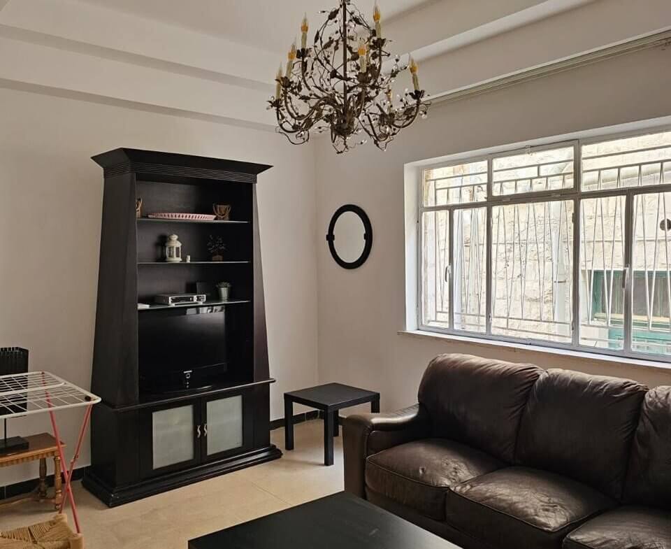a792e942-8a30-4a23-89f4-75fea91ac633 Living room with a black entertainment cabinet, brown leather sofa, and a crystal chandelier overhead.