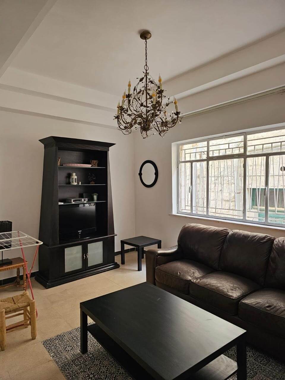a792e942-8a30-4a23-89f4-75fea91ac633 Living room with a black entertainment cabinet, brown leather sofa, and a crystal chandelier overhead.