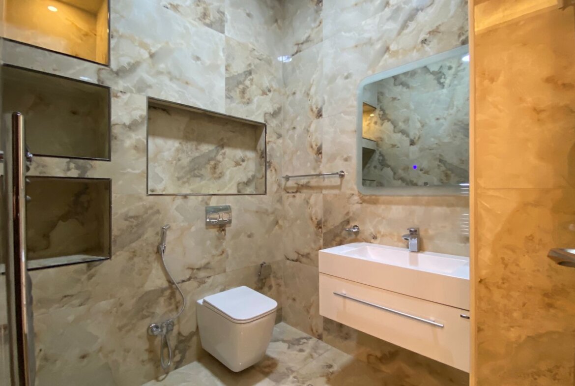 Modern marble bathroom with wall-mounted sink, floating drawers, and a wall-hung toilet; glass shower on left and large mirror above the sink.